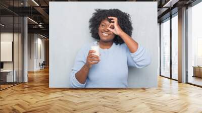 Young african american woman over grey grunge wall drinking a glass of milk with happy face smiling doing ok sign with hand on eye looking through fingers Wall mural