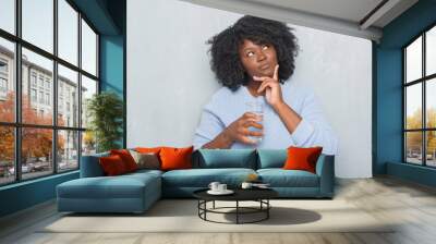 Young african american woman over grey grunge wall drinking a glass of water serious face thinking about question, very confused idea Wall mural