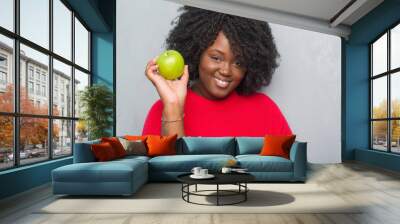 Young african american woman over grey grunge wall eating green apple with a happy face standing and smiling with a confident smile showing teeth Wall mural