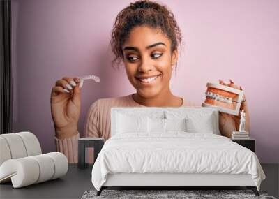 Young african american woman smiling happy holding professional orthodontic denture with metal braces and removable invisible aligner. Comparation of two dental straighten treatments Wall mural