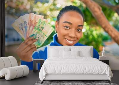 Young african american woman smiling happy holding south african rands banknotes at the park. Wall mural