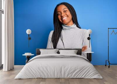 Young african american woman standing wearing casual turtleneck over blue isolated background happy face smiling with crossed arms looking at the camera. Positive person. Wall mural