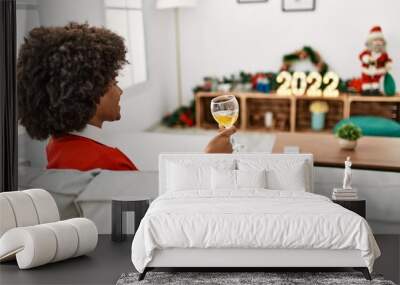 Young african american woman toasting with wine sitting by christmas decor at home Wall mural