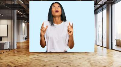 Young african american woman wearing casual clothes amazed and surprised looking up and pointing with fingers and raised arms. Wall mural