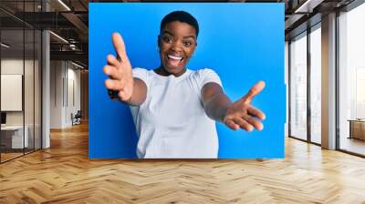 Young african american woman wearing casual white t shirt looking at the camera smiling with open arms for hug. cheerful expression embracing happiness. Wall mural