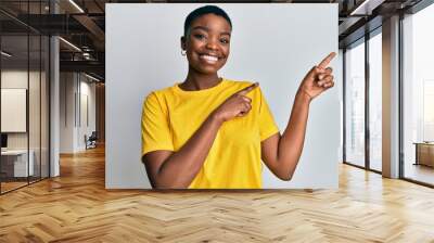 Young african american woman wearing casual yellow t shirt smiling and looking at the camera pointing with two hands and fingers to the side. Wall mural