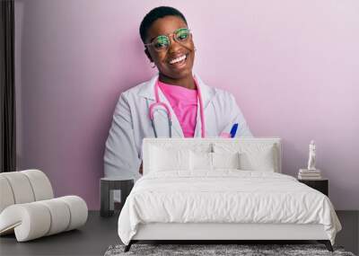 Young african american woman wearing doctor uniform and stethoscope winking looking at the camera with sexy expression, cheerful and happy face. Wall mural