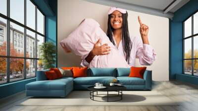 Young african american woman wearing pajama and eye mask hugging bed pillow surprised with an idea or question pointing finger with happy face, number one Wall mural