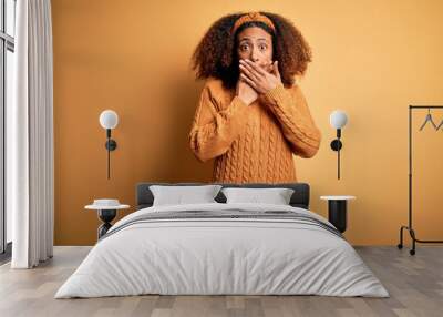 Young african american woman with afro hair wearing casual sweater over yellow background shocked covering mouth with hands for mistake. Secret concept. Wall mural