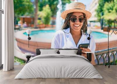 Young african american woman with braids smiling happy using smartphone outdoors on a sunny day of summer Wall mural