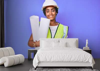 Young african american woman with braids wearing safety helmet holding blueprints looking positive and happy standing and smiling with a confident smile showing teeth Wall mural