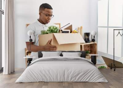 Young african man fired holding box with personal items at business office Wall mural