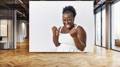 Young african woman standing over white isolated background very happy and excited doing winner gesture with arms raised, smiling and screaming for success. celebration concept. Wall mural