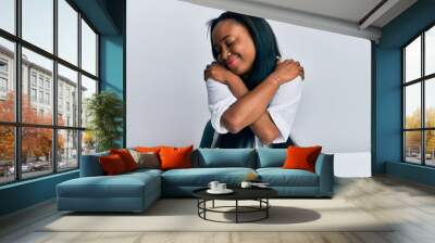 Young african woman wearing casual clothes sitting on the table hugging oneself happy and positive, smiling confident. self love and self care Wall mural