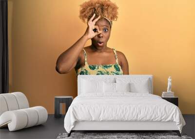 Young african woman with afro hair wearing summer dress doing ok gesture shocked with surprised face, eye looking through fingers. unbelieving expression. Wall mural