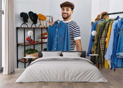 Young arab man customer holding shirt shopping at clothing store Wall mural