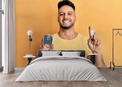 Young arab man holding canned food smiling with an idea or question pointing finger with happy face, number one Wall mural