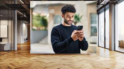 Young arab man smiling confident using smartphone at street Wall mural