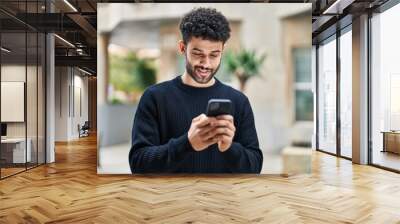 Young arab man smiling confident using smartphone at street Wall mural