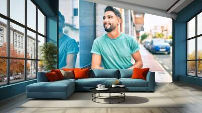 Young arab man smiling happy leaning on the wall at the city. Wall mural