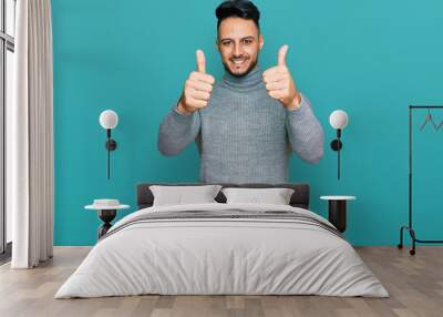 Young arab man wearing casual clothes approving doing positive gesture with hand, thumbs up smiling and happy for success. winner gesture. Wall mural