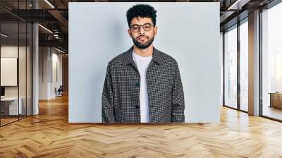 Young arab man with beard wearing glasses relaxed with serious expression on face. simple and natural looking at the camera. Wall mural