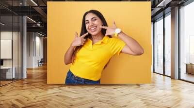 Young arab woman standing over yellow background smiling cheerful showing and pointing with fingers teeth and mouth. dental health concept. Wall mural