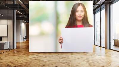 Young asian woman holding banner over isolated background with a confident expression on smart face thinking serious Wall mural