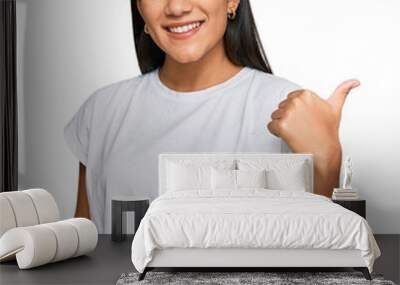 Young asian woman wearing casual white t shirt smiling with happy face looking and pointing to the side with thumb up. Wall mural