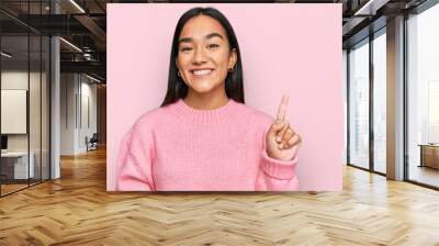 Young asian woman wearing casual winter sweater showing and pointing up with finger number one while smiling confident and happy. Wall mural