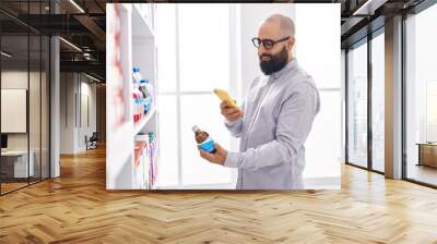 Young bald man customer make photo by smartphone to medicine bottle at pharmacy Wall mural