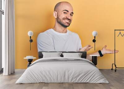 Young bald man wearing casual white t shirt inviting to enter smiling natural with open hand Wall mural