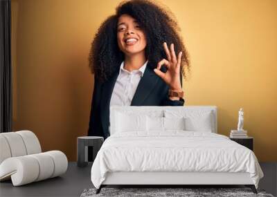 Young beautiful african american business woman with afro hair wearing elegant jacket smiling positive doing ok sign with hand and fingers. Successful expression. Wall mural