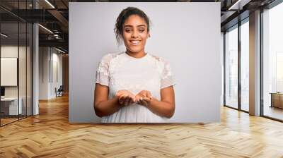 Young beautiful african american girl wearing casual t-shirt standing over white background Smiling with hands palms together receiving or giving gesture. Hold and protection Wall mural