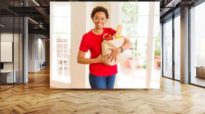 Young beautiful african american woman holding paper bag full of fresh healthy groceries Wall mural