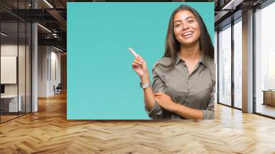 Young beautiful arab woman over isolated background with a big smile on face, pointing with hand and finger to the side looking at the camera. Wall mural