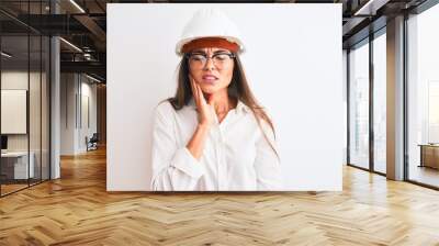 Young beautiful architect woman wearing helmet and glasses over isolated white background touching mouth with hand with painful expression because of toothache or dental illness on teeth Wall mural