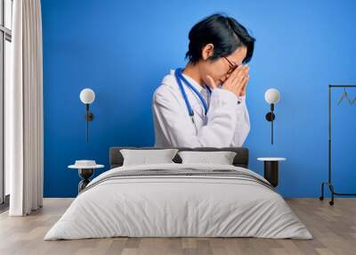 Young beautiful asian doctor girl wearing stethoscope and coat with blue cancer ribbon with sad expression covering face with hands while crying. Depression concept. Wall mural