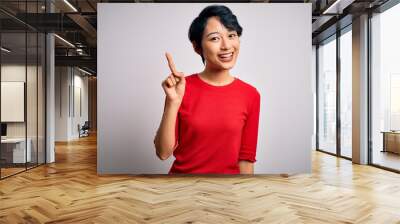 Young beautiful asian girl wearing casual red t-shirt standing over isolated white background pointing finger up with successful idea. Exited and happy. Number one. Wall mural