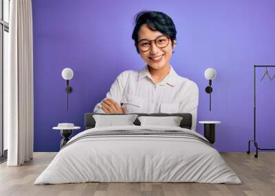 Young beautiful asian girl wearing casual shirt and glasses standing over purple background happy face smiling with crossed arms looking at the camera. Positive person. Wall mural