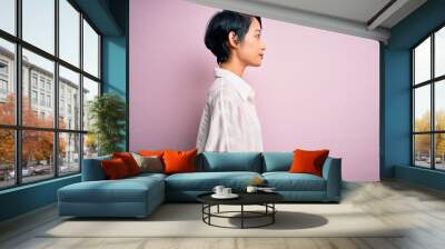 Young beautiful asian girl wearing casual shirt standing over isolated pink background looking to side, relax profile pose with natural face and confident smile. Wall mural