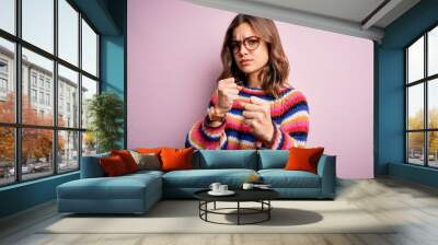 Young beautiful blonde girl wearing glasses and casual sweater over pink isolated background Ready to fight with fist defense gesture, angry and upset face, afraid of problem Wall mural