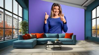 Young beautiful blonde woman wearing casual t-shirt over isolated purple background success sign doing positive gesture with hand, thumbs up smiling and happy. Cheerful expression and winner gesture. Wall mural