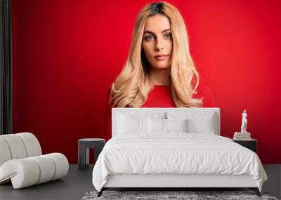 Young beautiful blonde woman wearing casual t-shirt standing over isolated red background Relaxed with serious expression on face. Simple and natural looking at the camera. Wall mural