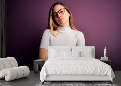 Young beautiful blonde woman with blue eyes wearing casual t-shirt over purple background skeptic and nervous, disapproving expression on face with crossed arms. Negative person. Wall mural