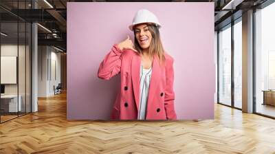 Young beautiful brunette architect woman wearing safety helmet over pink background smiling doing phone gesture with hand and fingers like talking on the telephone. Communicating concepts. Wall mural