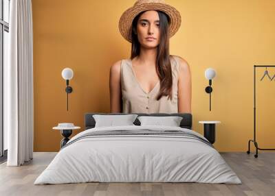 Young beautiful brunette woman on vacation wearing casual dress and hat Relaxed with serious expression on face. Simple and natural looking at the camera. Wall mural