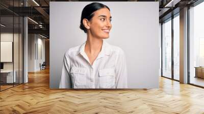 Young beautiful brunette woman wearing casual shirt over isolated white background looking away to side with smile on face, natural expression. Laughing confident. Wall mural