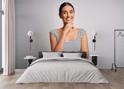 Young beautiful brunette woman wearing casual striped dress over isolated white background looking confident at the camera smiling with crossed arms and hand raised on chin. Thinking positive. Wall mural