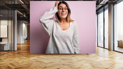 Young beautiful brunette woman wearing casual sweater and glasses over pink background confuse and wonder about question. Uncertain with doubt, thinking with hand on head. Pensive concept. Wall mural